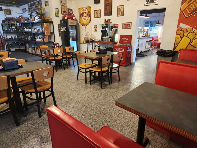 Retro-style diner interior with red booths, wooden tables, vintage Coca-Cola machines, and epoxy flake flooring