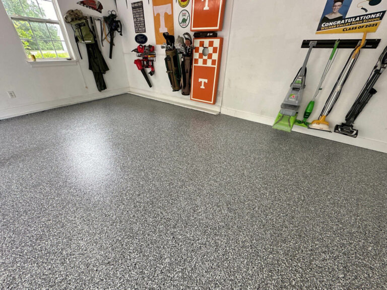 Gray epoxy flake garage floor with glossy finish in a residential garage featuring organized tools, wall decor, and natural light from a window