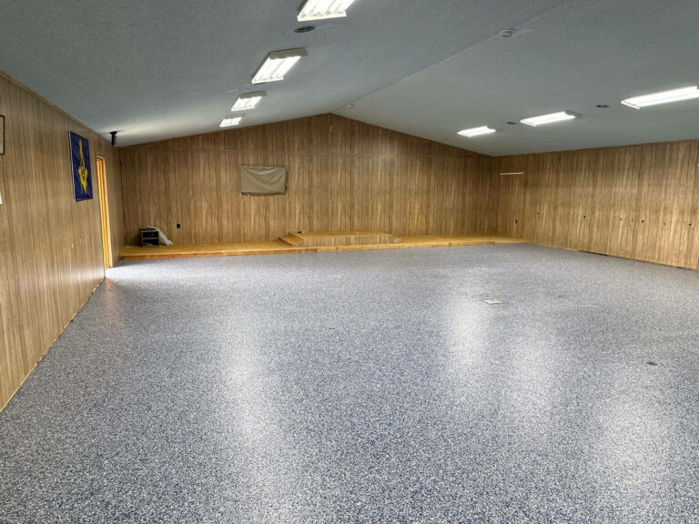Large multipurpose room with wood-paneled walls and seamless gray epoxy flake flooring