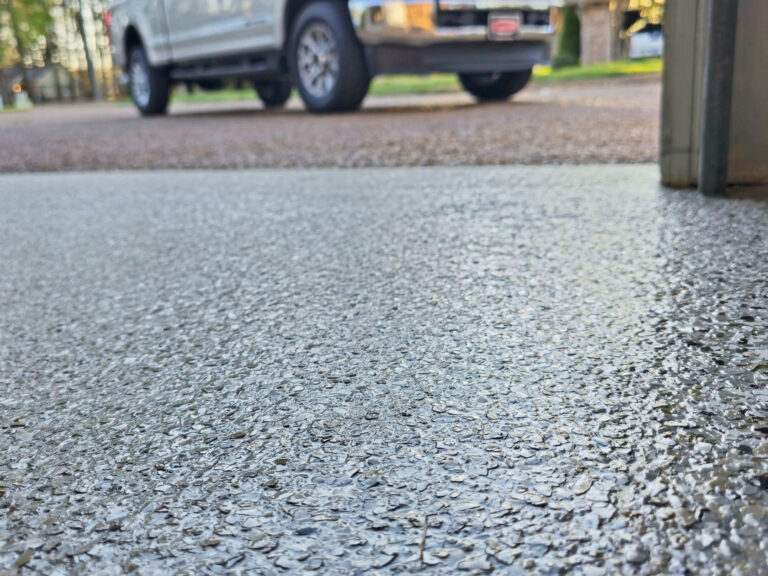 Wet epoxy flake garage floor showing glossy, textured surface durability with a parked truck in the background