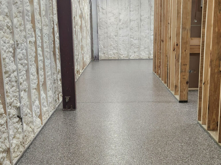 Basement under construction with spray foam insulation and gray epoxy flake flooring installed by Elite Floor Solutions