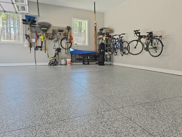 Epoxy flake garage floor with light gray finish in a modern residential garage featuring wall-mounted bikes, organized storage, and natural lighting