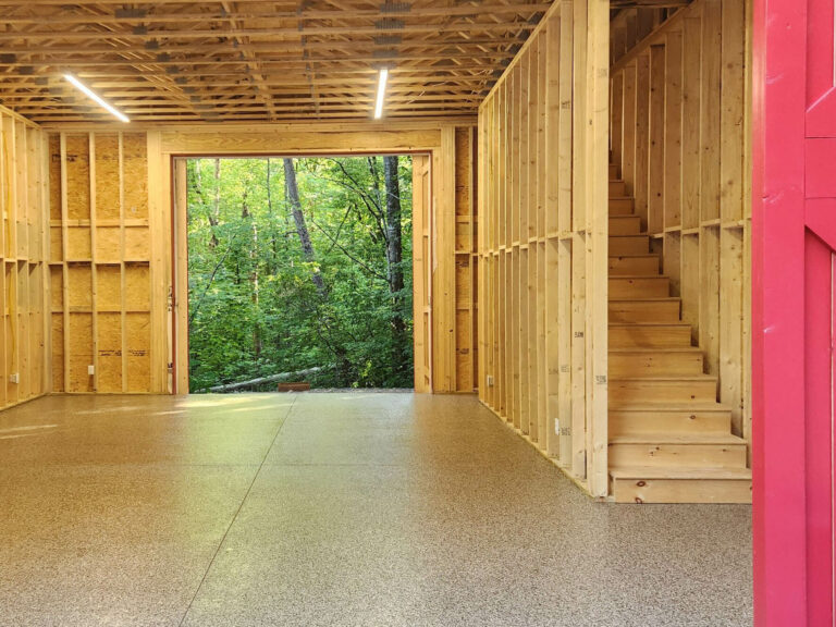 New construction interior with unfinished wood framing and tan epoxy flake flooring
