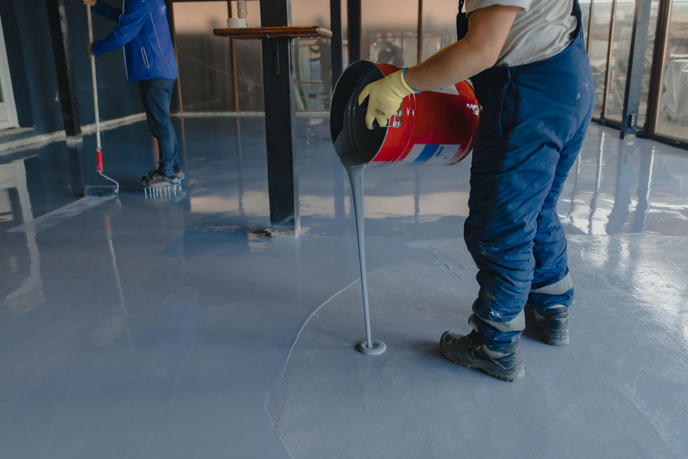 Epoxy resin being poured and rolled onto concrete subfloor during professional installation process for commercial flooring