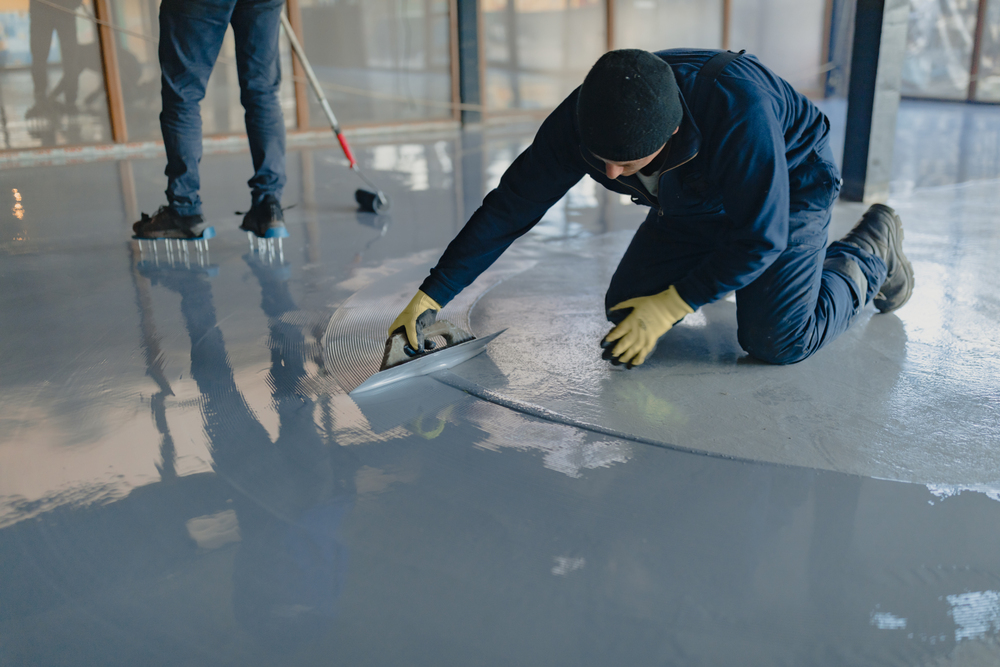 Flooring technician applying smooth epoxy coating on concrete floor using trowel during installation
