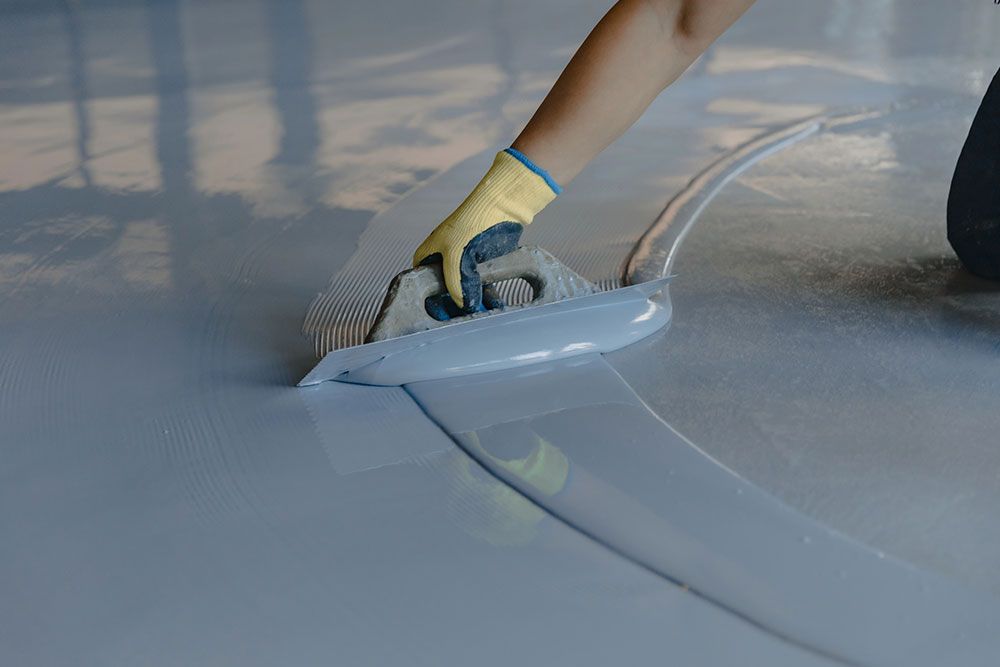 Flooring technician applying smooth epoxy coating on concrete floor using trowel during installation