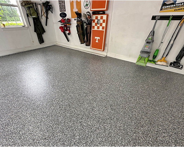 Residential garage with gray epoxy flake flooring and organized wall storage featuring sports and cleaning equipment