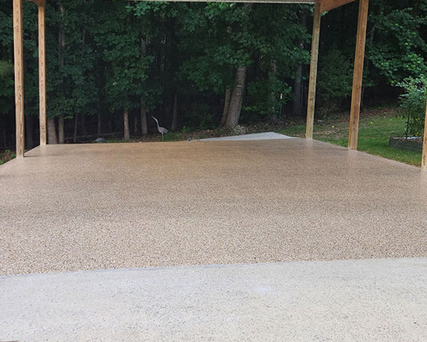 Tan epoxy flake patio coating installed under outdoor pergola with concrete apron