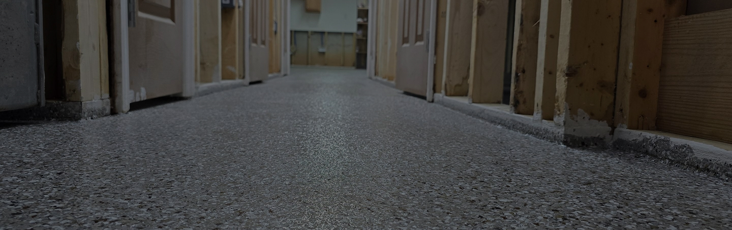 Light gray epoxy flake floor installed in commercial hallway with unfinished walls during renovation
