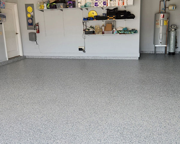 Light gray epoxy flake floor installed in a clean residential garage with storage shelves