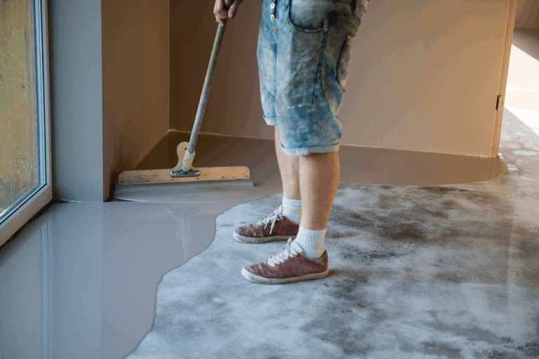 Technician applying epoxy floor coating using squeegee for smooth, self-leveling finish during installation