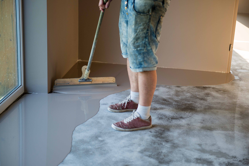 Technician applying epoxy floor coating using squeegee for smooth, self-leveling finish during installation
